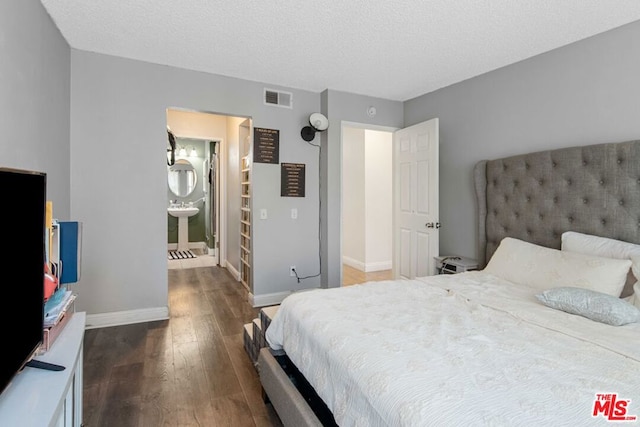 bedroom with a textured ceiling, connected bathroom, and dark wood-type flooring