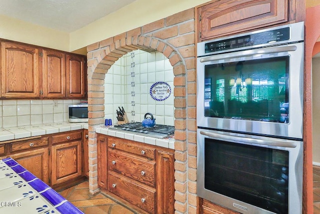 kitchen featuring decorative backsplash, stainless steel appliances, and tile counters