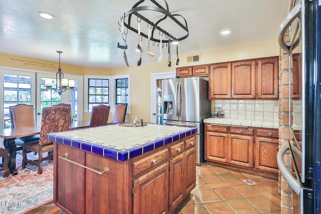 kitchen featuring stainless steel fridge, refrigerator, tasteful backsplash, a center island, and tile counters