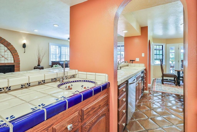 kitchen featuring tile countertops, sink, stainless steel dishwasher, and dark tile patterned flooring