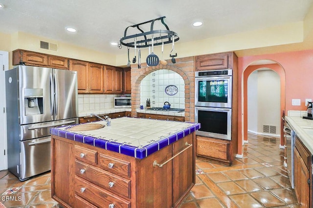 kitchen with decorative backsplash, appliances with stainless steel finishes, sink, tile countertops, and a kitchen island