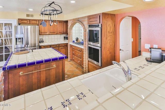 kitchen featuring a center island, tasteful backsplash, tile countertops, decorative light fixtures, and appliances with stainless steel finishes