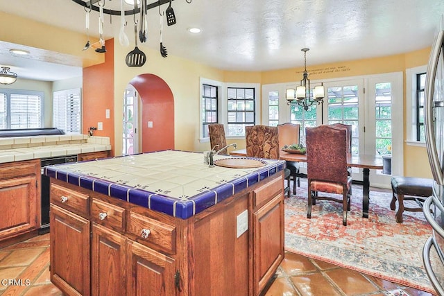 kitchen with sink, pendant lighting, tile countertops, a notable chandelier, and a kitchen island