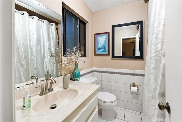 bathroom with toilet, vanity, wainscoting, tile patterned flooring, and tile walls