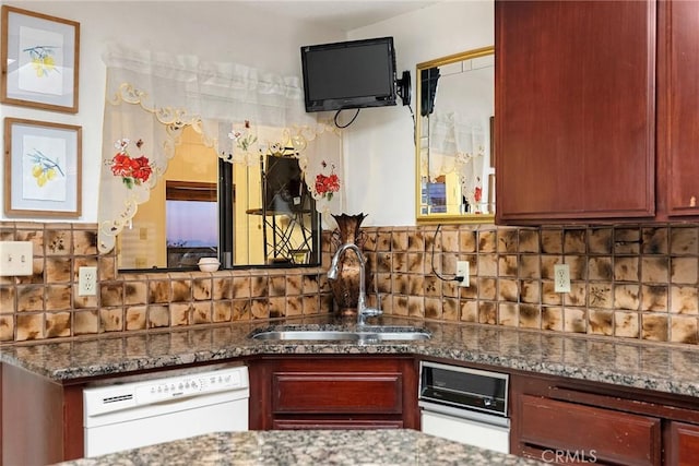 kitchen with white dishwasher, decorative backsplash, a sink, and dark stone counters