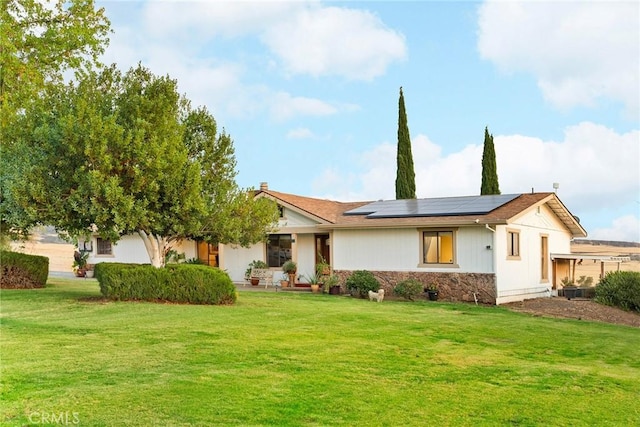 ranch-style house with stone siding, a front lawn, and roof mounted solar panels