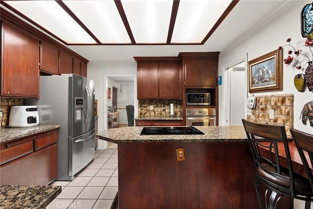 kitchen featuring light tile patterned floors, dark stone countertops, backsplash, a peninsula, and appliances with stainless steel finishes