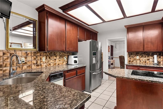 kitchen with stainless steel fridge, dark stone countertops, a sink, backsplash, and light tile patterned floors