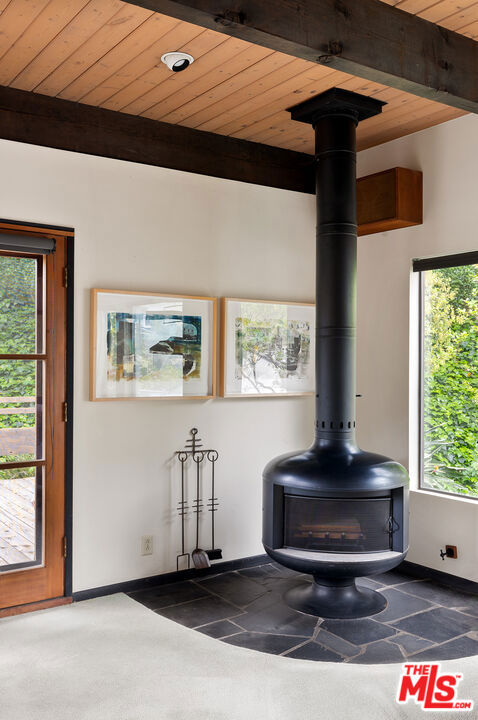 unfurnished living room featuring beam ceiling, a wood stove, and a wealth of natural light