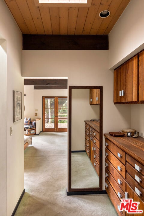 interior space with wood ceiling, a skylight, light carpet, and beamed ceiling