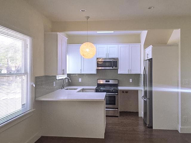 kitchen featuring sink, stainless steel appliances, white cabinets, decorative light fixtures, and kitchen peninsula