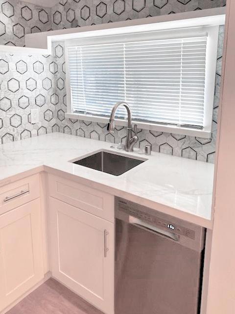 kitchen featuring dishwasher, light stone countertops, sink, and white cabinets