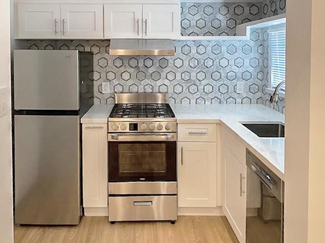 kitchen with sink, stainless steel appliances, tasteful backsplash, white cabinets, and wall chimney exhaust hood