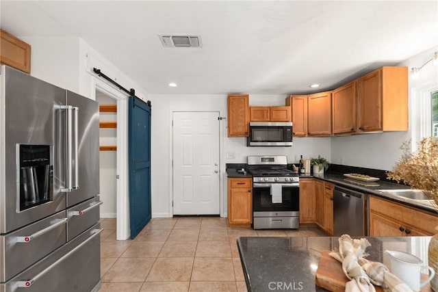 kitchen featuring light tile patterned floors, stainless steel appliances, a barn door, and sink