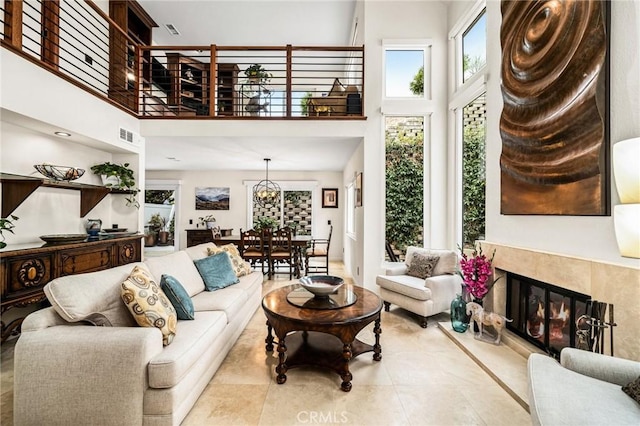 living area featuring visible vents, a towering ceiling, a high end fireplace, tile patterned floors, and an inviting chandelier