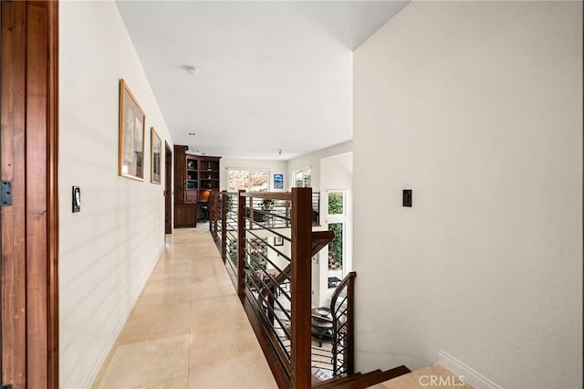 corridor featuring baseboards, light tile patterned flooring, and an upstairs landing