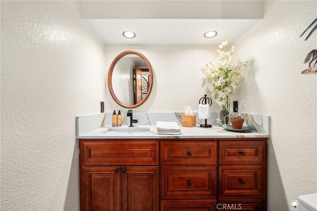 bathroom featuring toilet, a textured wall, and vanity