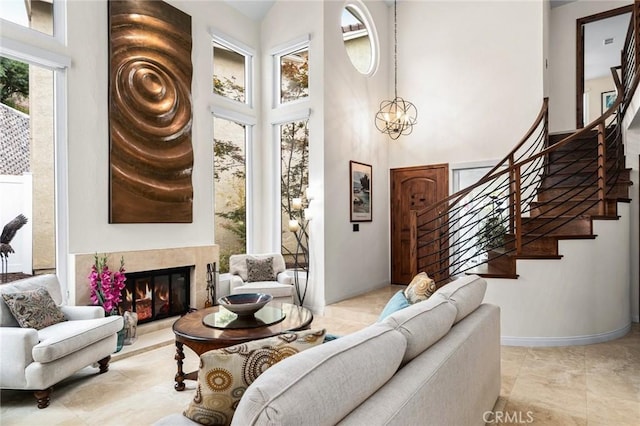 living area featuring a notable chandelier, a high ceiling, a premium fireplace, baseboards, and stairs