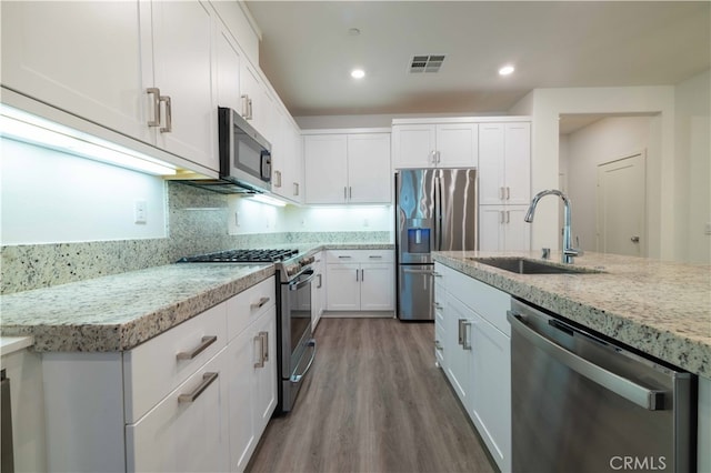 kitchen featuring appliances with stainless steel finishes, white cabinetry, light stone counters, wood-type flooring, and sink