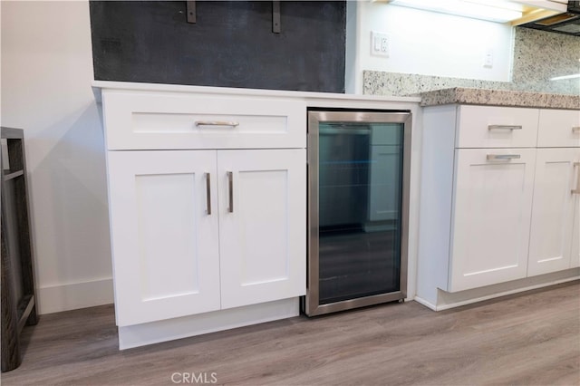 kitchen featuring white cabinets, beverage cooler, light wood-type flooring, and light stone countertops