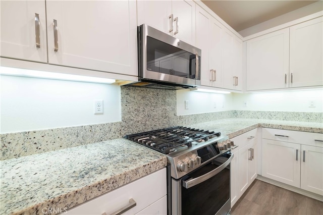 kitchen with light stone countertops, stainless steel appliances, white cabinetry, and light wood-type flooring