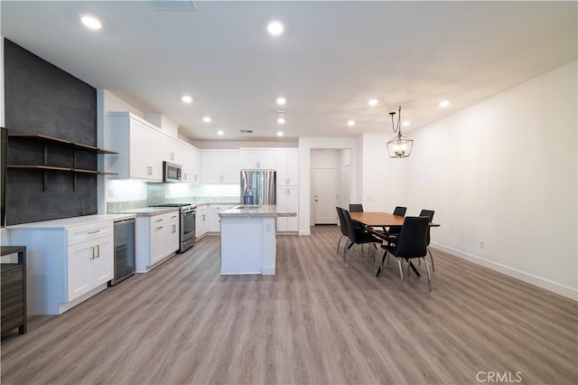 kitchen with appliances with stainless steel finishes, wine cooler, white cabinets, a kitchen island, and light hardwood / wood-style flooring