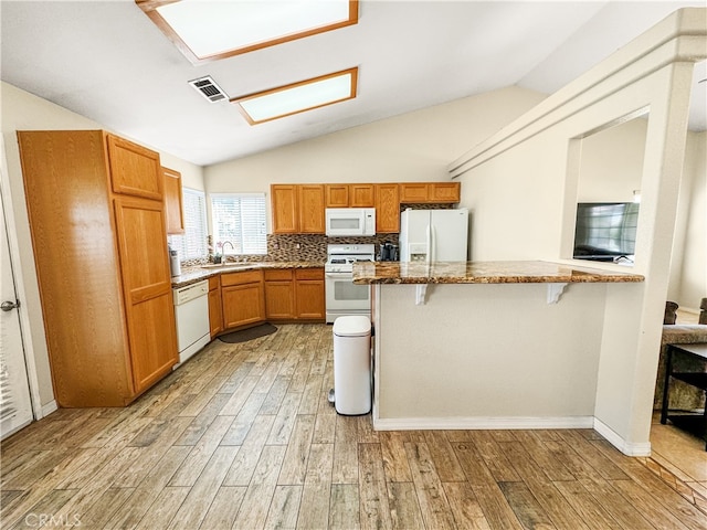 kitchen with lofted ceiling, sink, white appliances, a breakfast bar area, and light wood-type flooring