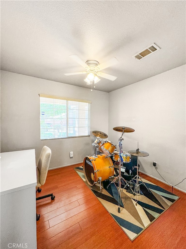 exercise room featuring ceiling fan, hardwood / wood-style flooring, and a textured ceiling