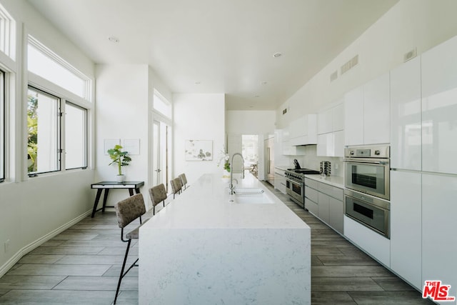 kitchen with white cabinetry, dark wood-type flooring, a breakfast bar, stainless steel appliances, and sink