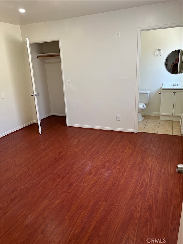 unfurnished bedroom with connected bathroom, hardwood / wood-style floors, sink, and a closet