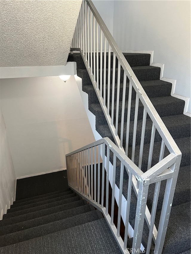 stairway featuring a textured ceiling and carpet flooring