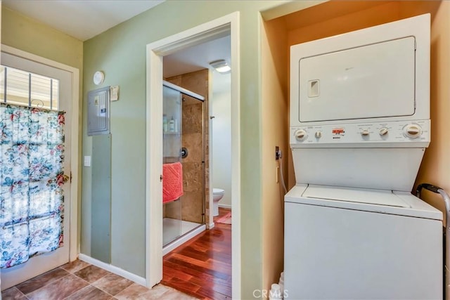 washroom featuring wood finished floors, baseboards, laundry area, electric panel, and stacked washer / dryer