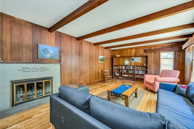 living room with beamed ceiling, light wood-type flooring, wooden walls, and a brick fireplace