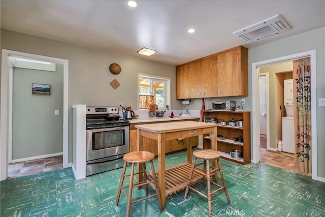 kitchen featuring baseboards, stacked washing maching and dryer, stainless steel electric stove, recessed lighting, and light countertops