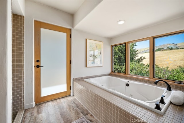 bathroom featuring tiled tub, a mountain view, and hardwood / wood-style flooring