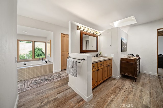 bathroom featuring a relaxing tiled tub, wood-type flooring, and vanity