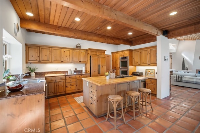 kitchen featuring beamed ceiling, wood counters, sink, stainless steel double oven, and a kitchen island