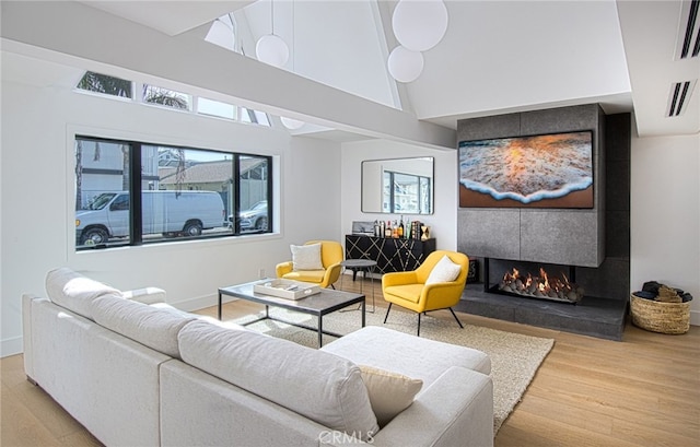 living room featuring hardwood / wood-style floors, high vaulted ceiling, and a tiled fireplace