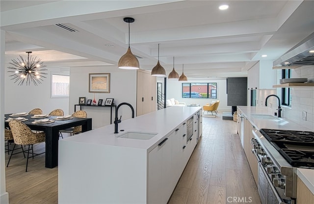 kitchen with sink, pendant lighting, a center island with sink, light hardwood / wood-style floors, and white cabinetry