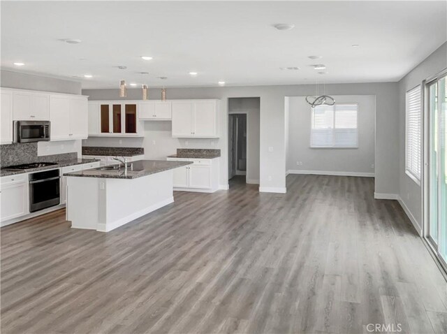 kitchen with hanging light fixtures, a center island with sink, dark stone countertops, appliances with stainless steel finishes, and white cabinets