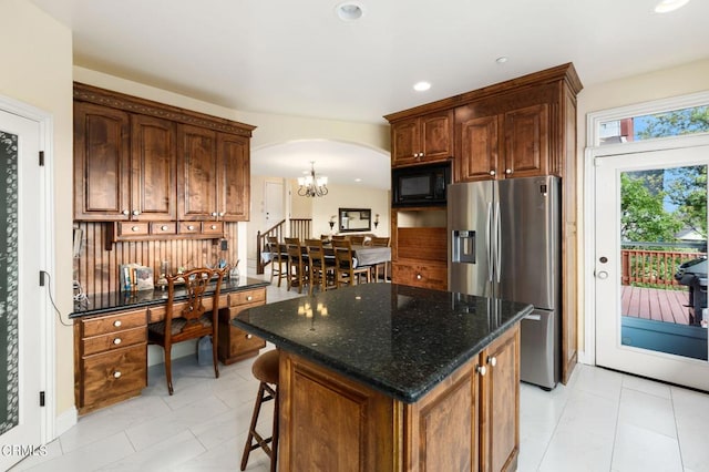 kitchen with stainless steel fridge, a kitchen island, black microwave, dark stone counters, and a notable chandelier