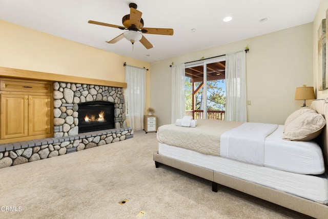 bedroom with a stone fireplace, light carpet, ceiling fan, and access to exterior