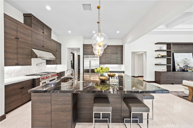 kitchen with a breakfast bar, pendant lighting, a large island with sink, sink, and wall chimney exhaust hood