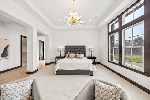 bedroom with a notable chandelier, light wood-type flooring, a raised ceiling, and a walk in closet