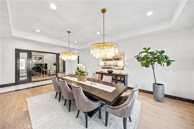 dining area featuring a raised ceiling, light hardwood / wood-style flooring, and a notable chandelier