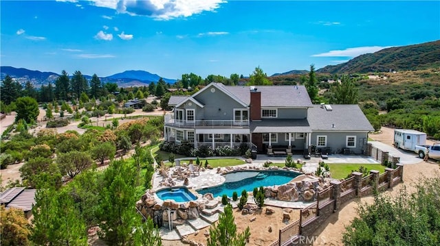 back of property featuring a balcony, outdoor lounge area, a swimming pool with hot tub, a patio area, and a mountain view