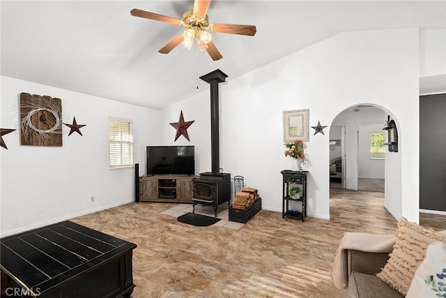 living room featuring ceiling fan, a wood stove, and vaulted ceiling