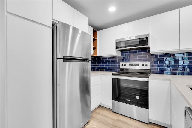 kitchen featuring stainless steel appliances, white cabinets, light hardwood / wood-style floors, and tasteful backsplash