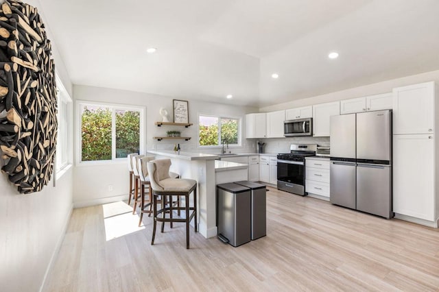 kitchen with a center island, a kitchen breakfast bar, appliances with stainless steel finishes, white cabinets, and light wood-type flooring