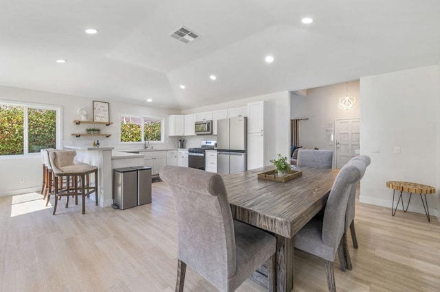 dining space with plenty of natural light, lofted ceiling, and light hardwood / wood-style flooring